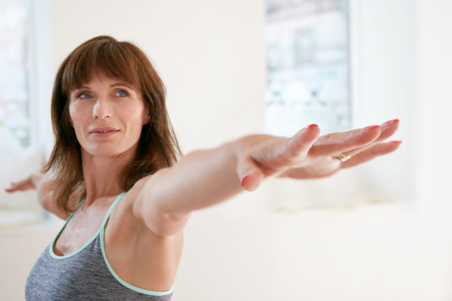 44972546 - portrait of fitness woman stretching her hands and looking away. attractive mature woman exercising yoga in virabhadrasana pose. female doing warrior pose in gym.
